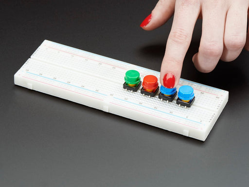 Top-down shot of 15 colorful round tactile button switches in green, yellow, red, blue, and white.