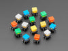 Angled  shot of 15 colorful square tactile button switches in green, yellow, red, blue, and white.