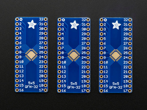 A pair of tweezers holding a microchip hovers over the SMT Breakout PCB for 32-QFN or 32-TQFP placement on a long blue rectangular breakout board.