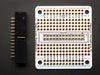 A white manicured hand holds up an assembled Adafruit Small-Size Perma-Proto Raspberry Pi Breadboard PCB.