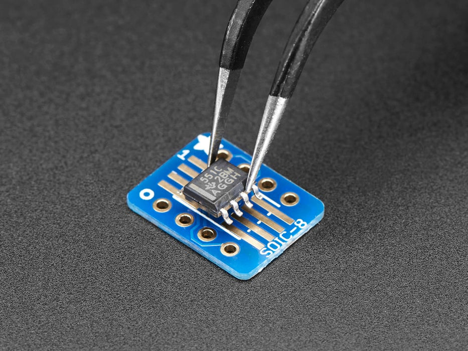 A pair of tweezers holding a microchip hovers over the SMT Breakout PCB for SOIC-8, MSOP-8 or TSSOP-8.