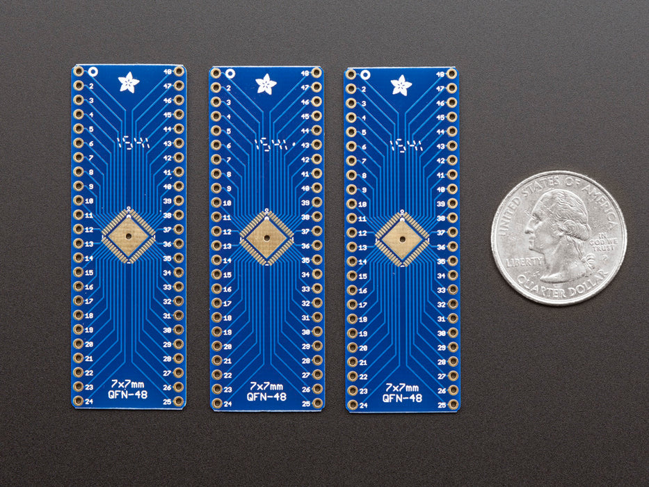 A pair of tweezers holding a microchip hovers over the SMT Breakout PCB for 48-QFN or 48-TQFP placement on a long blue rectangular breakout board.