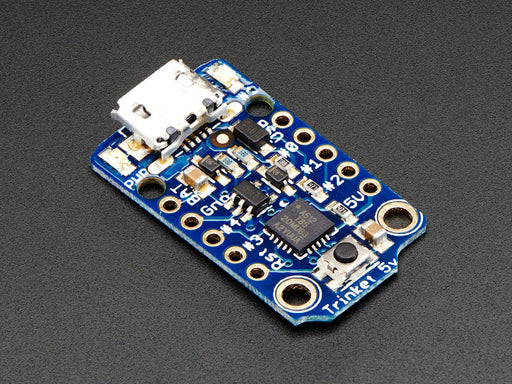 Hand holding Adafruit TriHand holding small Adafruit Trinket - Mini Microcontrollerket board.