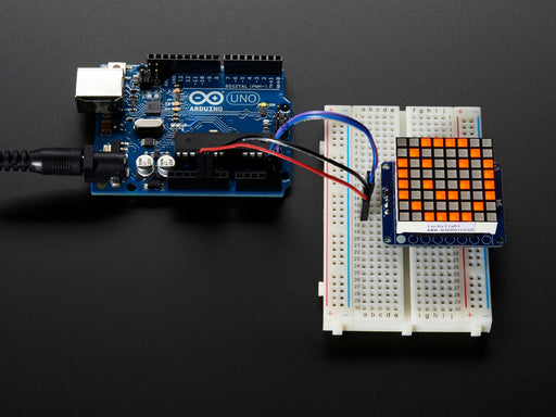 Close-up of Soldered and assembled Small 1.2" 8x8 Ultra Bright Square Amber LED Matrix + Backpack on a breadboard powered by an Arduino Uno. The LED Matrix displays an orange smiley.