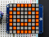 Close-up of Soldered and assembled Small 1.2" 8x8 Ultra Bright Square Amber LED Matrix + Backpack on a breadboard powered by an Arduino Uno. The LED Matrix displays an orange smiley.