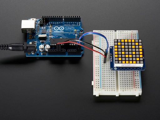 Soldered and assembled Small 1.2" 8x8 Ultra Bright Square yellow LED Matrix + Backpack on a breadboard powered by an Arduino Uno. The LED Matrix displays a yellow smiley.