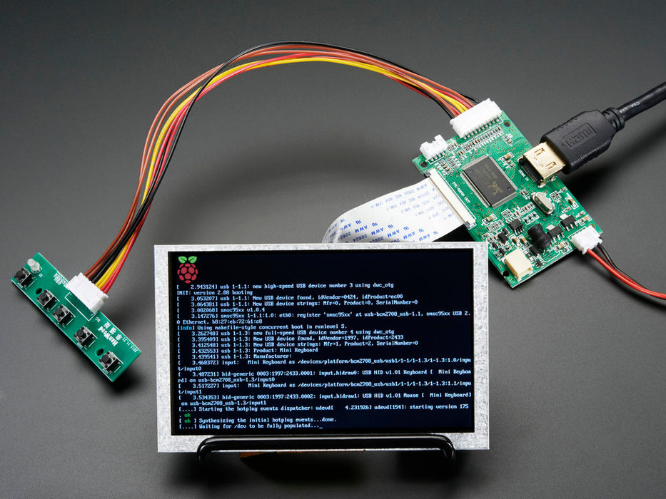 Angled shot of an assembled HDMI 4 Pi: 5" Display (no Touch) w/Mini Driver. The HDMI screen displays a desktop image including the Adafruit logo, the Raspberry Pi logo, and a pink heart.