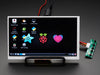 Angled shot of a HDMI 4 Pi: 7" Display (no Touch) w/Mini Driver. The monitor displays a desktop background with a adafruit logo, raspberry logo, and a heart. 