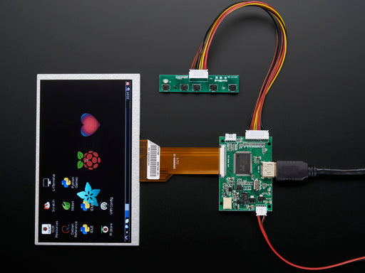 Angled shot of a HDMI 4 Pi: 7" Display (no Touch) w/Mini Driver. The monitor displays a desktop background with a adafruit logo, raspberry logo, and a heart. 