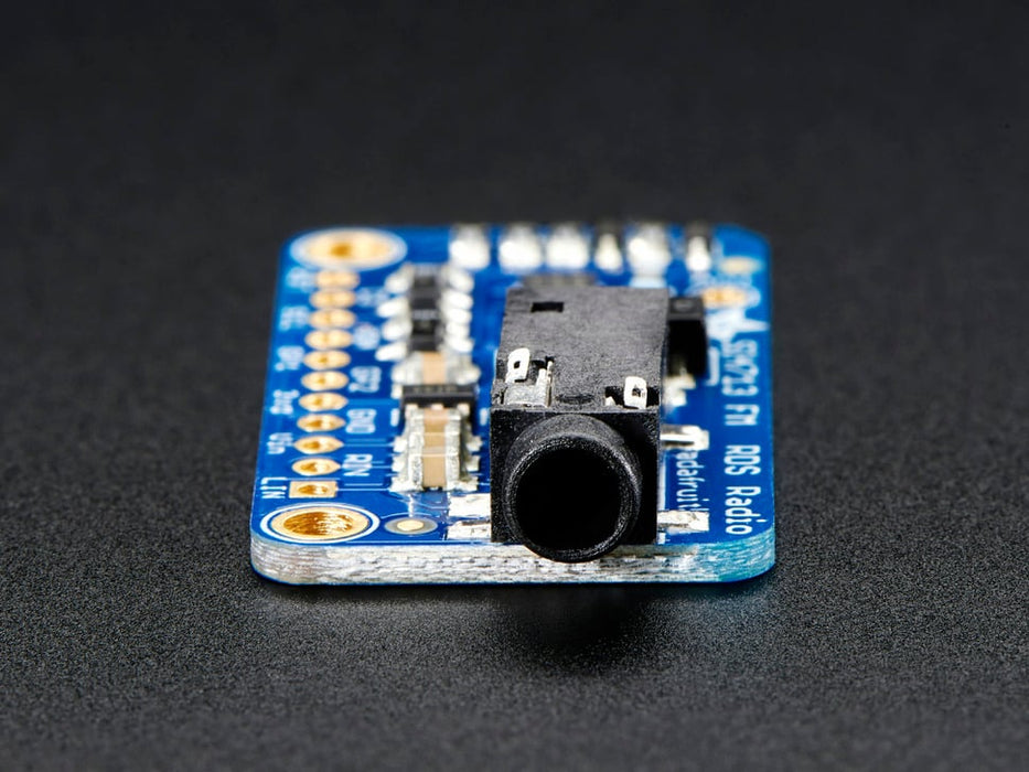 Top down view of a Adafruit Stereo FM Transmitter with RDS/RBDS Breakout next to a 11-pin header and under blue string coiled up.