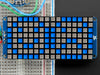 Close-up of Soldered and assembled 16x8 1.2" LED Matrix + Backpack - Ultra Bright Square Blue LEDs on a breadboard. The LED Matrices display a smiling emoji and a frowning emoji.