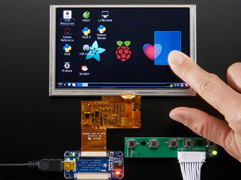 Angled shot of an assembled HDMI 4 Pi: 5" Display w/Touch and Mini Driver. The HDMI screen displays a desktop image including the Adafruit logo, the Raspberry Pi logo, and a pink heart.