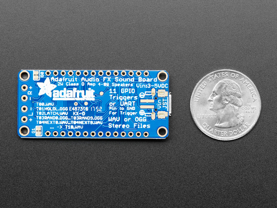 A long blue rectangular audio FX sound board assembled onto two half-size breadboards. The board is wired up to a 3 x AA battery pack and two speakers. A white hand presses a row of small tactile buttons wired up to the audio board.