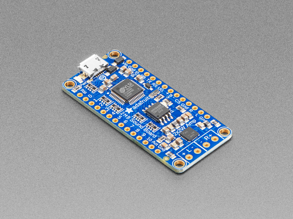 A long blue rectangular audio FX sound board assembled onto two half-size breadboards. The board is wired up to a 3 x AA battery pack and two speakers. A white hand presses a row of small tactile buttons wired up to the audio board.