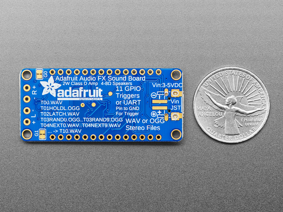 A long blue rectangular audio FX sound board assembled onto two half-size breadboards. The board is wired up to a 3 x AA battery pack and two speakers. A white hand presses a row of small tactile buttons wired up to the audio board.