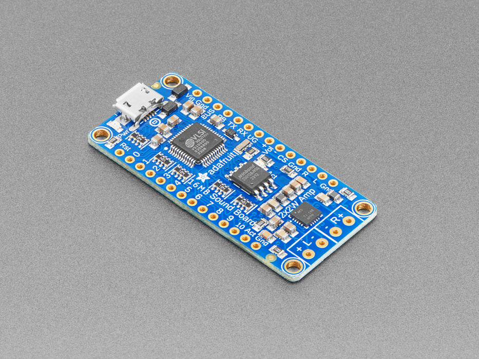 A long blue rectangular audio FX sound board assembled onto two half-size breadboards. The board is wired up to a 3 x AA battery pack and two speakers. A white hand presses a row of small tactile buttons wired up to the audio board.