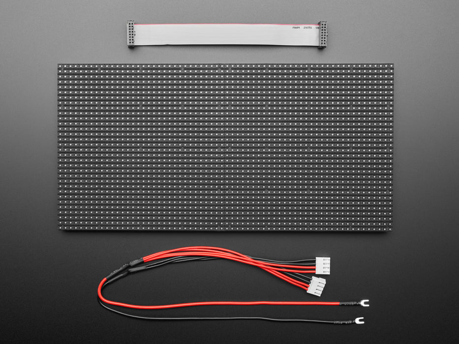 Two white hands hold out an assembled and powered on 64x32 RGB LED Matrix Panel - 5mm pitch. The matrix displays "Adafruit Industries LED MATRIX! 32x64 *RGB*"