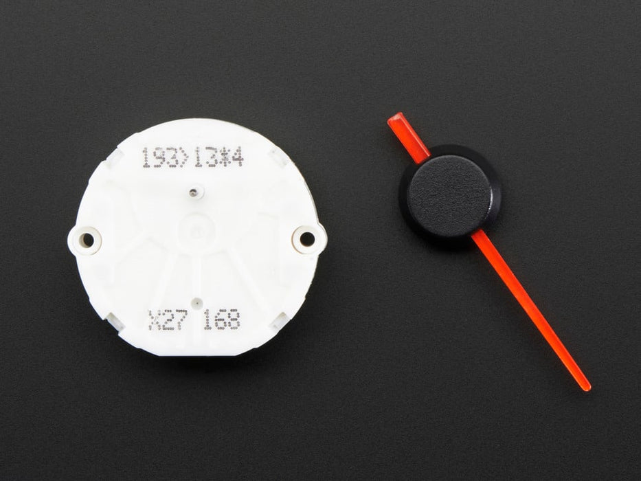 Close up of a Automotive Gauge Stepper Motor connected to a half sized white bread board, spinning. 