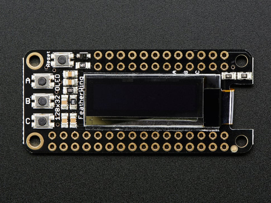 Angled shot of a Adafruit FeatherWing OLED - 128x32 OLED Add-on For Feather connected to a white breadboard and a lithium battery. 