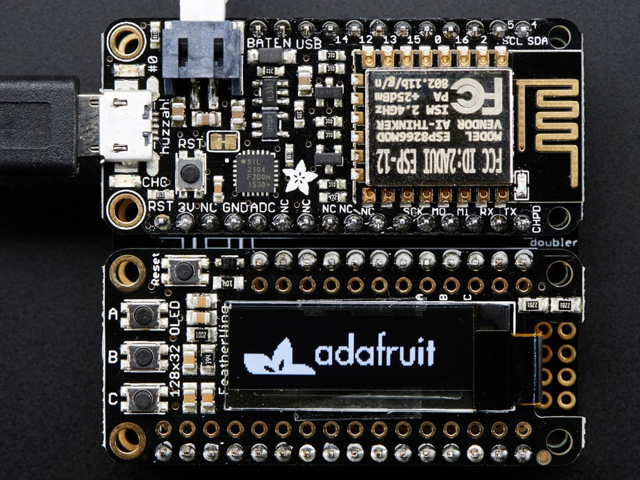 Angled shot of a Adafruit FeatherWing OLED - 128x32 OLED Add-on For Feather connected to a white breadboard and a lithium battery. 