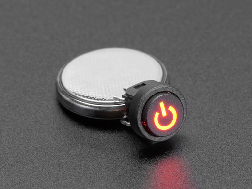 Close-up of a mini red illuminated push-button with a red power symbol installed in a half-size breadboard. Also are on the breadboard are two jumper wires and a resistor.