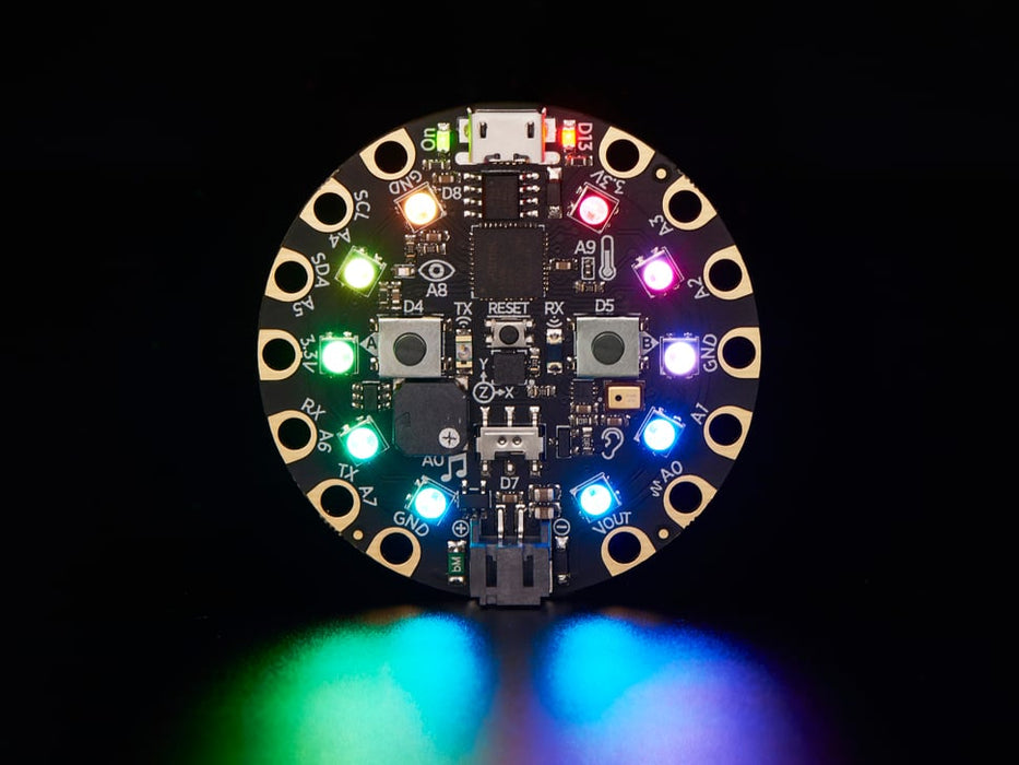 A Black woman's manicured hand holds a round microcontroller with lit up LEDs.