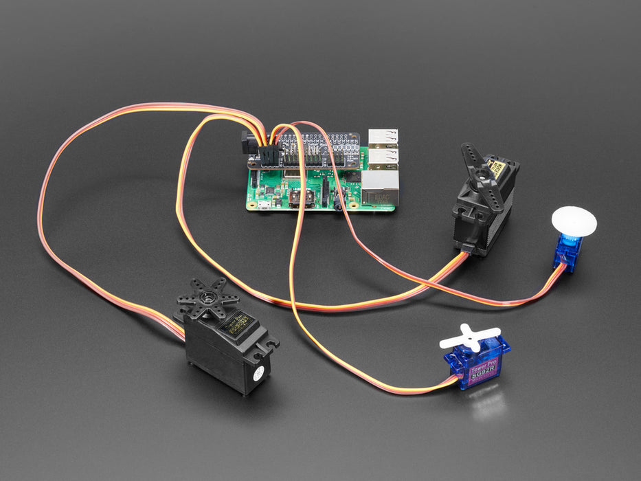 Angled shot of a Adafruit 16-Channel PWM / Servo Bonnet for Raspberry Pi stacked on a Raspberry Pi Zero connected to 4 different kinds of Servos. 