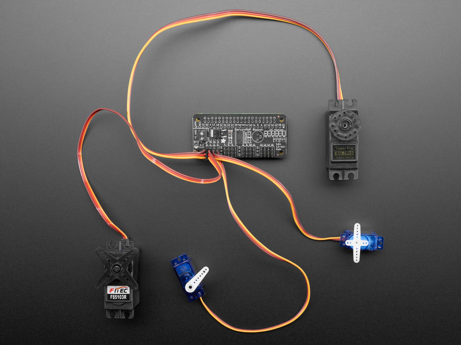 Angled shot of a Adafruit 16-Channel PWM / Servo Bonnet for Raspberry Pi stacked on a Raspberry Pi Zero connected to 4 different kinds of Servos. 