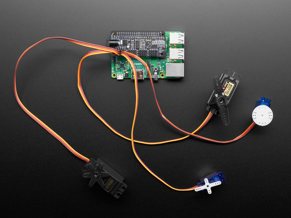 Angled shot of a Adafruit 16-Channel PWM / Servo Bonnet for Raspberry Pi stacked on a Raspberry Pi Zero connected to 4 different kinds of Servos. 