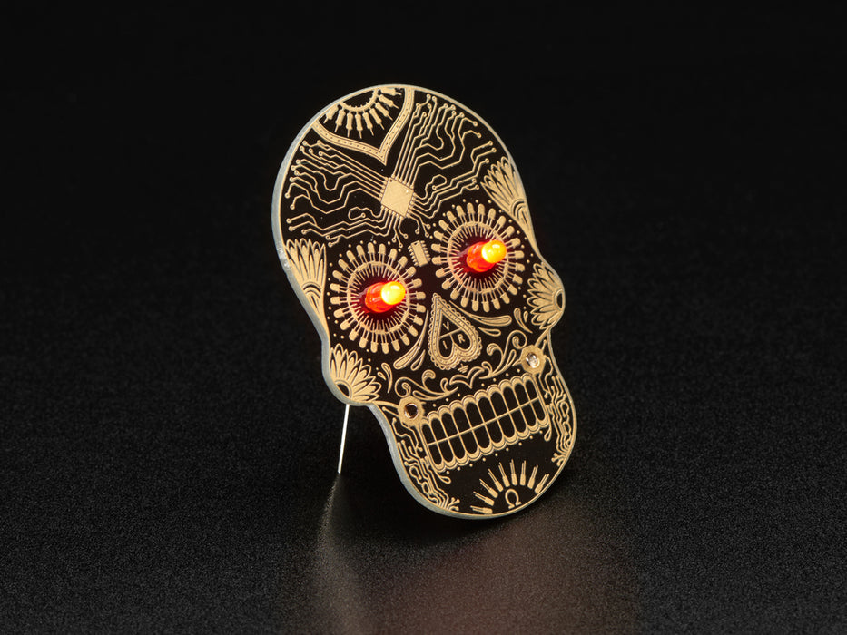 Angled shot of a Dia de los Muertos skull PCB with red glowing LEDs for eyes.