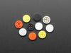 Angled shot of 10 plastic button caps colored reddish-orange, yellow, white, and black.