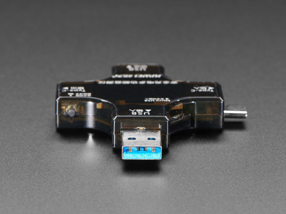 Top view of multifunctional USB tester connected to a laptop. The display reads voltage and current information.