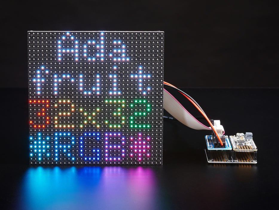 White woman wearing blue gloved rotating an RGB LED matrix. The LED animation resembles falling colored sand.