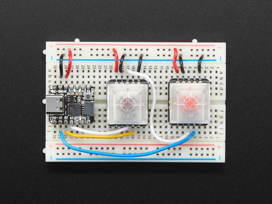 Video of breakout PCB installed on breadboard with key caps and switches. A finger reaches down to press the keys which light up rainbow colors.