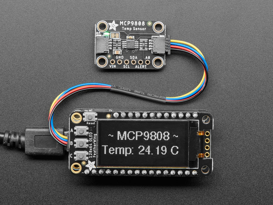 Top view of temperature sensor breakout above an OLED display FeatherWing. The OLED display reads "MCP9808 Temp: 24.19��C"