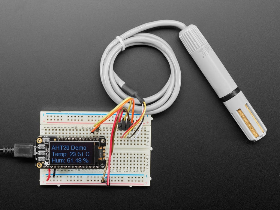 Top view of AM2315C sensor wired to a breadboard with an FeatherWing OLED display. The OLED shows the data from the temperature-humidity sensor.