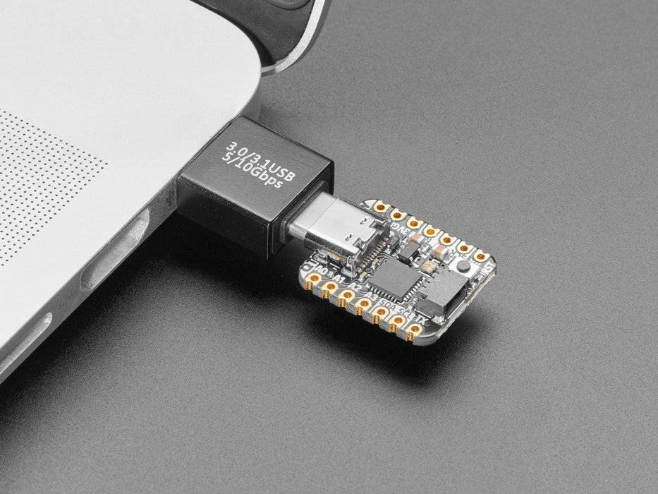 Angled video of a USB adapter plugged into a laptop. A square-shaped microcontroller is plugged into the other end of the adapter. An RGB LED on the microcontroller emits a rainbow spectrum of colors.