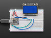 TFT display breakout soldered and assembled onto a half-size breadboard and wired up to a microcontroller. The color TFT screen displays a boot-up screen.