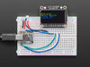 TFT display breakout soldered and assembled onto a half-size breadboard and wired up to a microcontroller. The color TFT screen displays a boot-up screen.