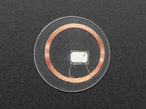 Bottom of small, clear, circular NTAG203 (13.56MHz RFID/NFC) tag next to US quarter for scale.