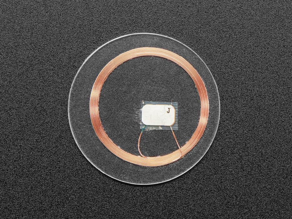 Bottom of small, clear, circular NTAG203 (13.56MHz RFID/NFC) tag next to US quarter for scale.