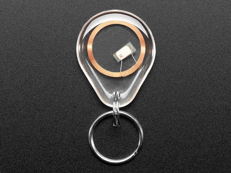 Overhead shot of a clear keychain fob with an RFID/NFC NTAG203 tag inside placed next to a US quarter for scale.