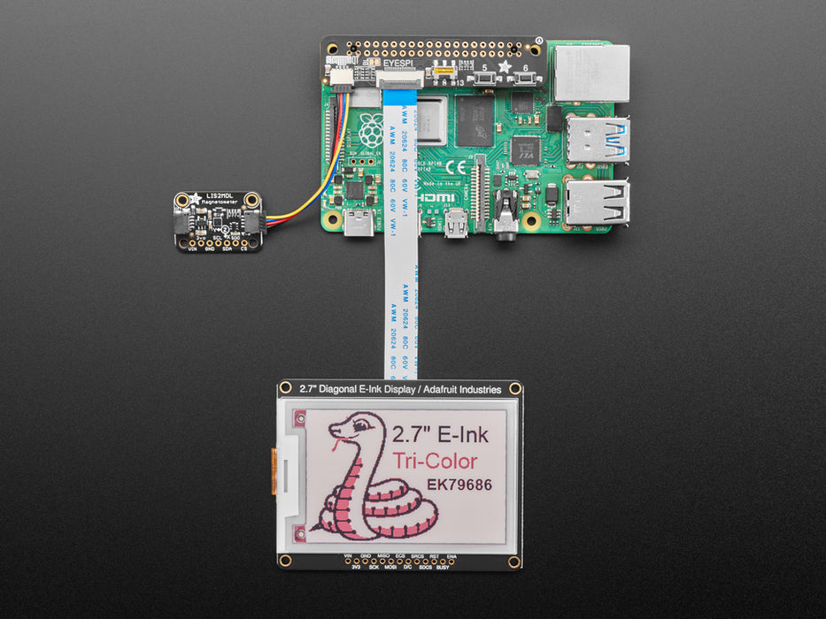 Overhead shot of long, black, slim add-on board installed on a Raspberry Pi computer and cabled to a sensor board and an electronic ink display.