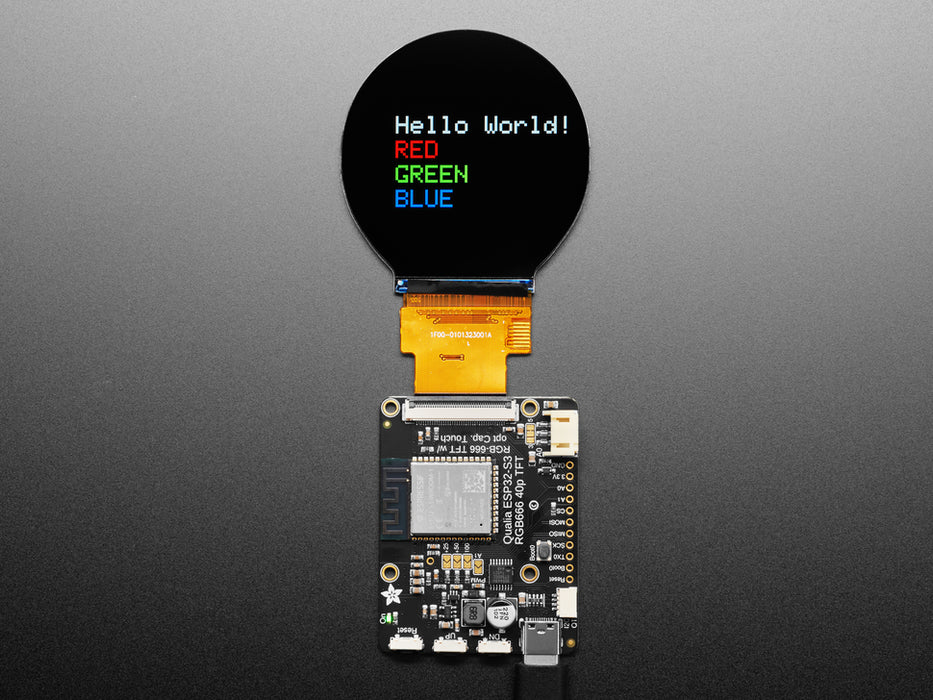 Overhead shot of round TFT display connected to a black, rectangular microcontroller. The TFT displays a rainbow color gradient.