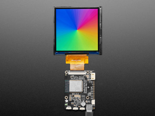 Overhead shot of a 3.4" square TFT screen connected to a microcontroller. The screen displays a colorful rainbow gradient. A white hand draws a heart on the screen.