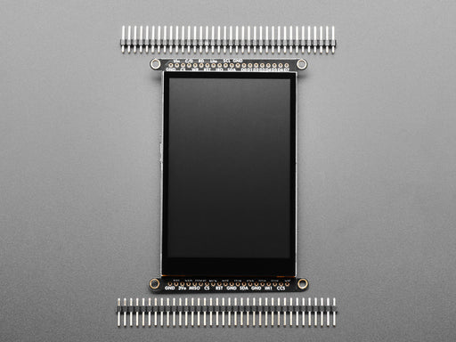 Overhead shot of a Black woman's green-manicured hand touching a 3.5" TFT display breakout connected to a small, square-shaped microcontroller. The TFT screen displays a drawn red heart.