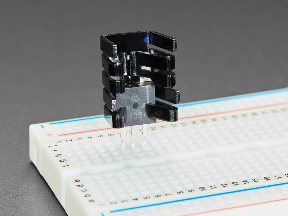 Clip on bent metal heat sink on top of a transistor, plugged into breadboard.