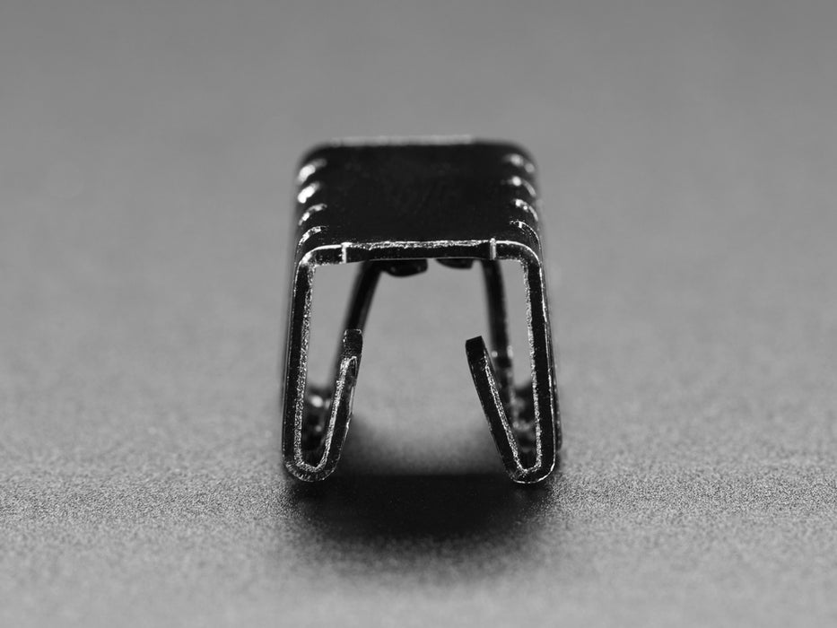 Clip on bent metal heat sink on top of a transistor, plugged into breadboard.